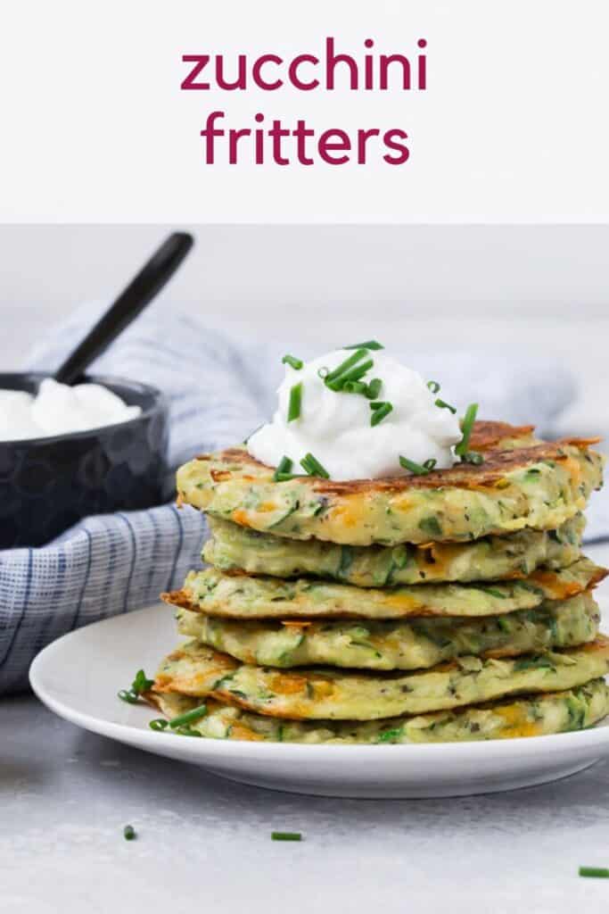 Stack of zucchini pancakes on a white plate, topped with sour cream and chives. Text overlay reads "zucchini fritters"