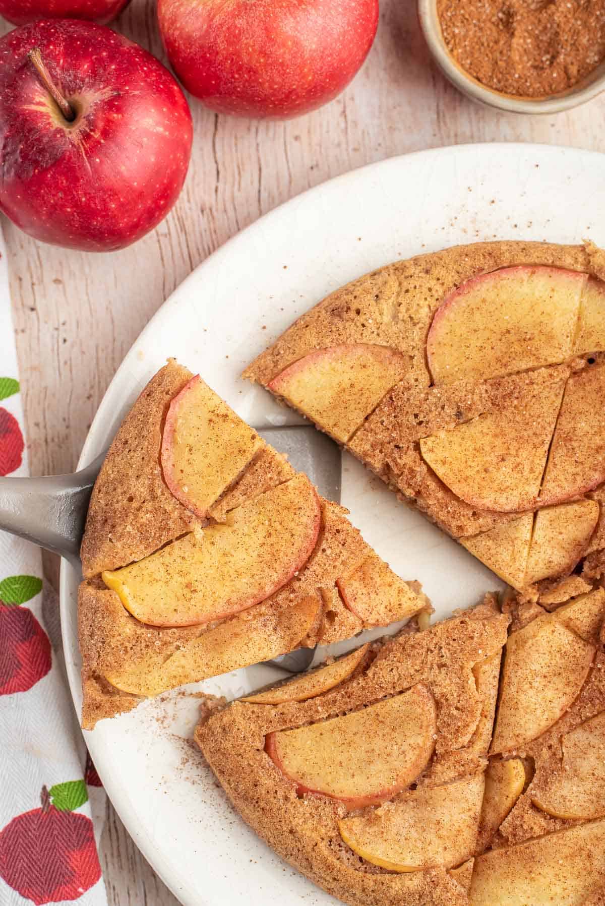 Slice of apple skillet pancake being removed from a plate with additional slices. 