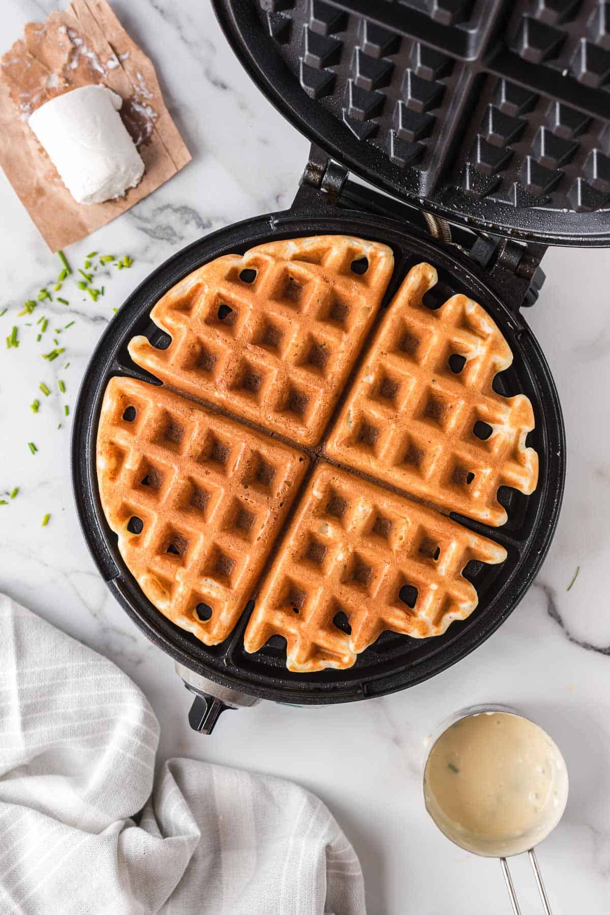 Overhead view of a waffle in a waffle iron, surrounded by ingredients.