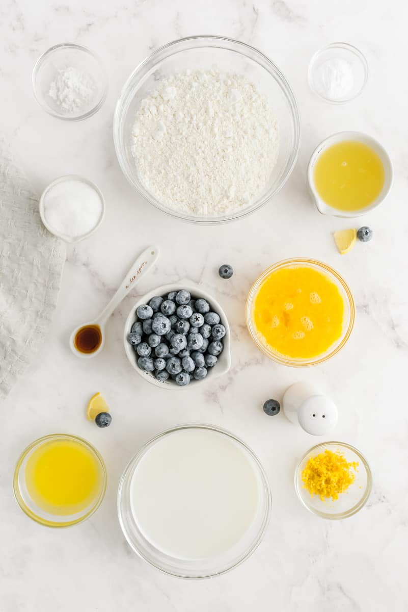 Ingredients for lemon pancakes with fresh blueberries. All  ingredients are in small clear glass bowls.