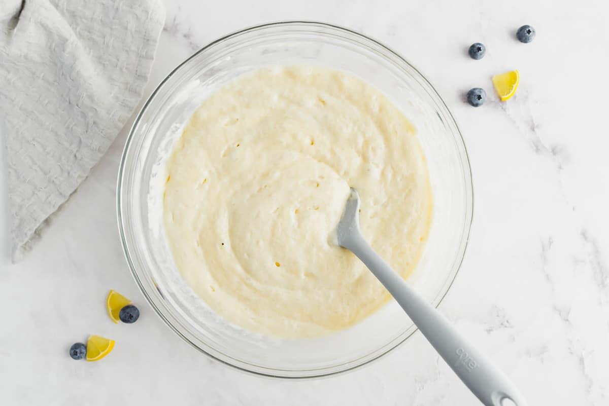 Lemon pancake batter in a glass bowl with a metal spoon.