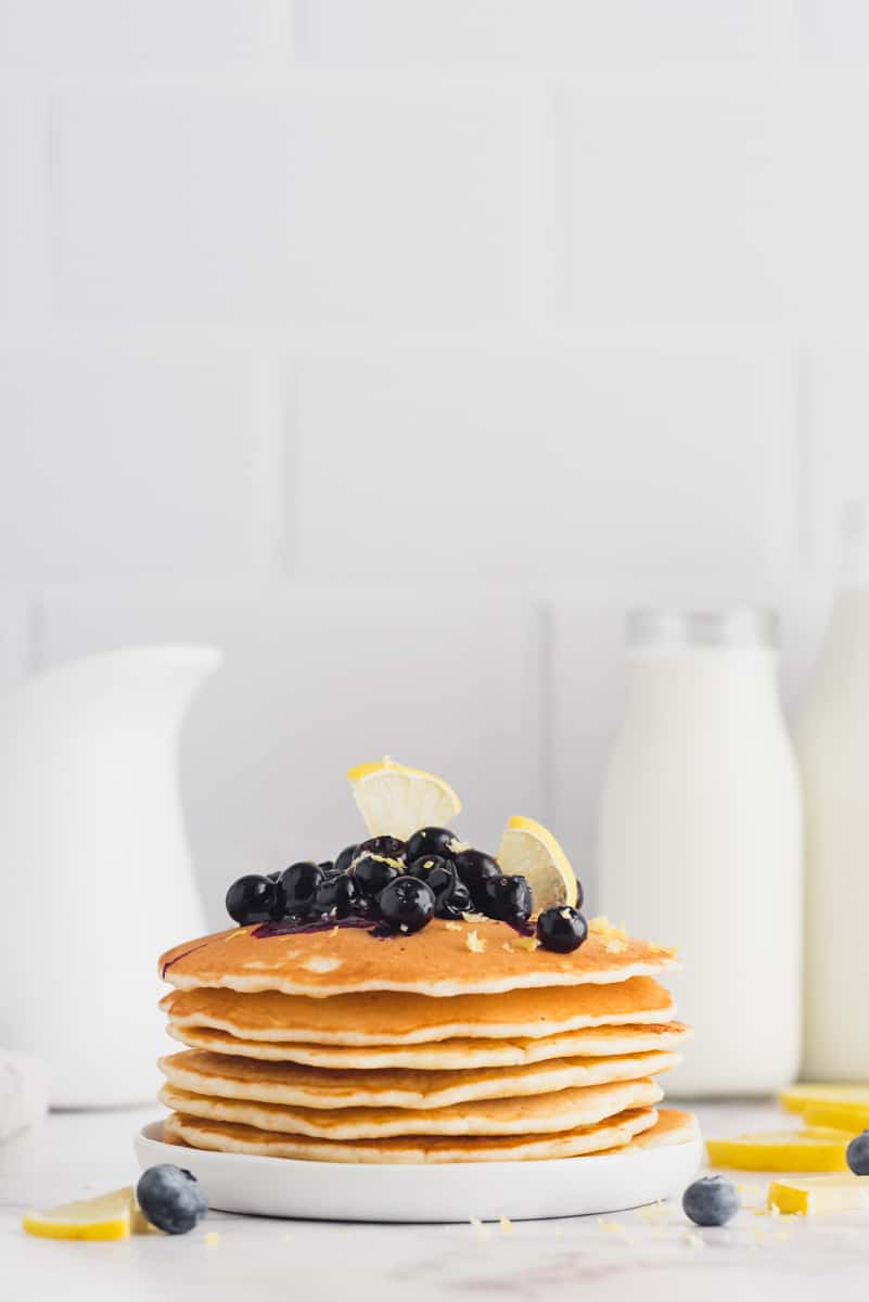 Stack of lemon pancakes with blueberries. Milk in background.