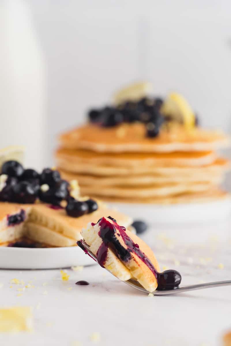 Pancakes on a fork with blueberries. More pancakes in the background.