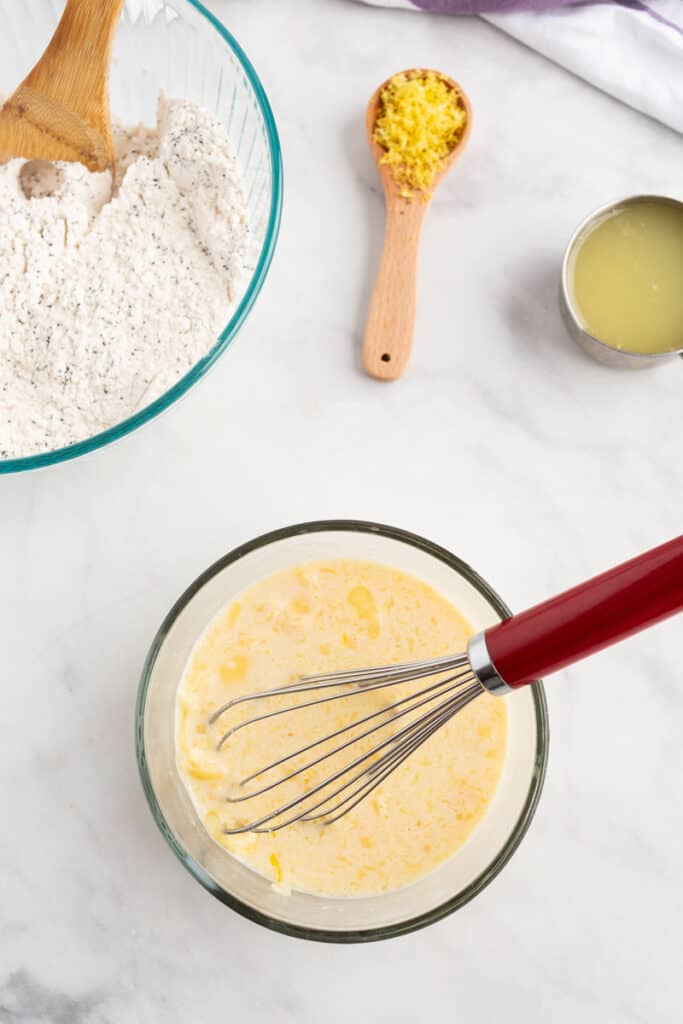 Wet ingredients for pancakes in a clear glass bowl with a whisk.