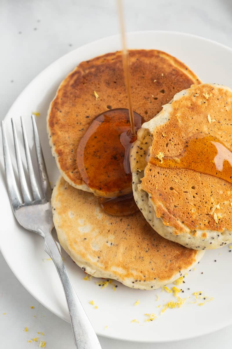 Three lemon pancakes on a plate with syrup and a fork.