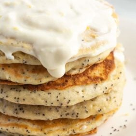 Stack of lemon poppyseed pancakes on a white plate, with a cream cheese glaze.