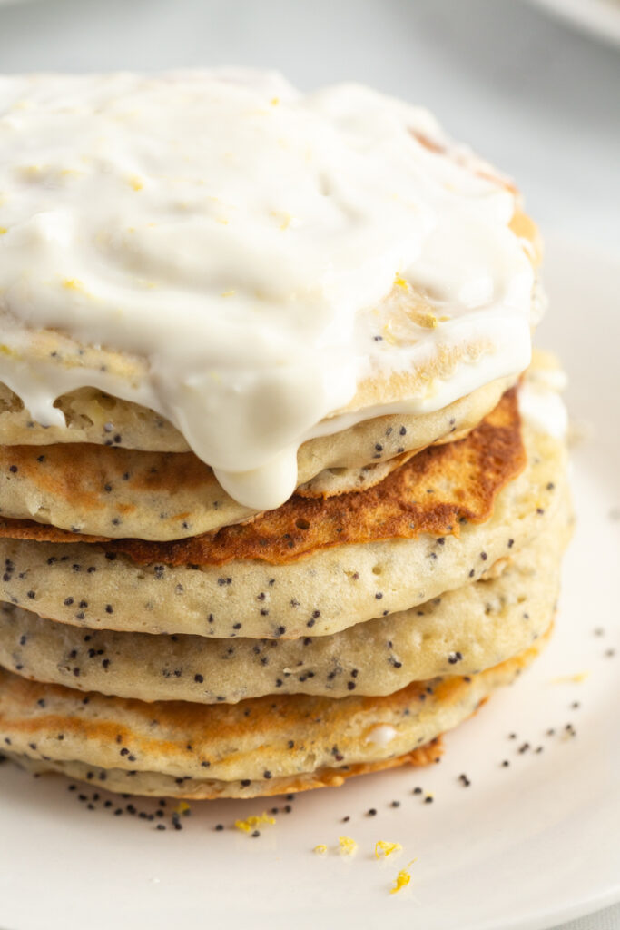 Stack of lemon poppyseed pancakes on a white plate, with a cream cheese glaze.