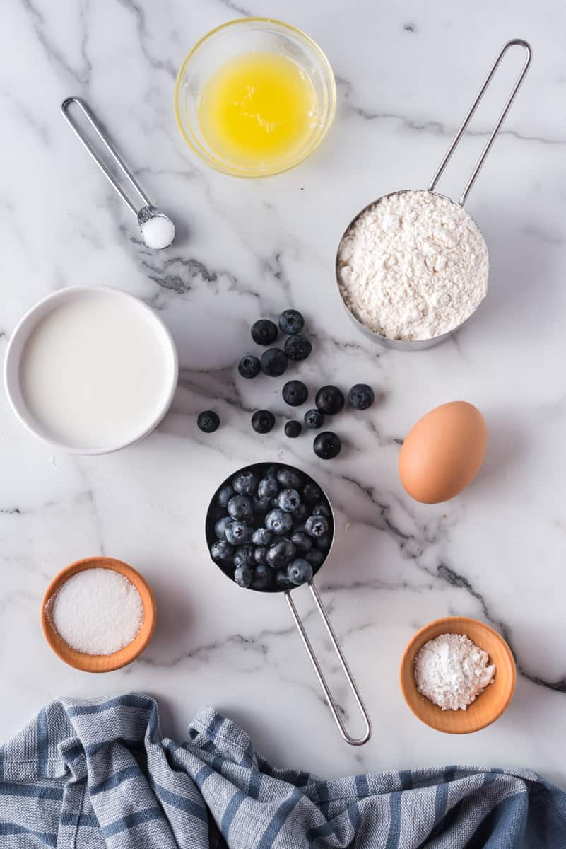 Overhead view of ingredients needed to make blueberry pancakes, on a white marble background.