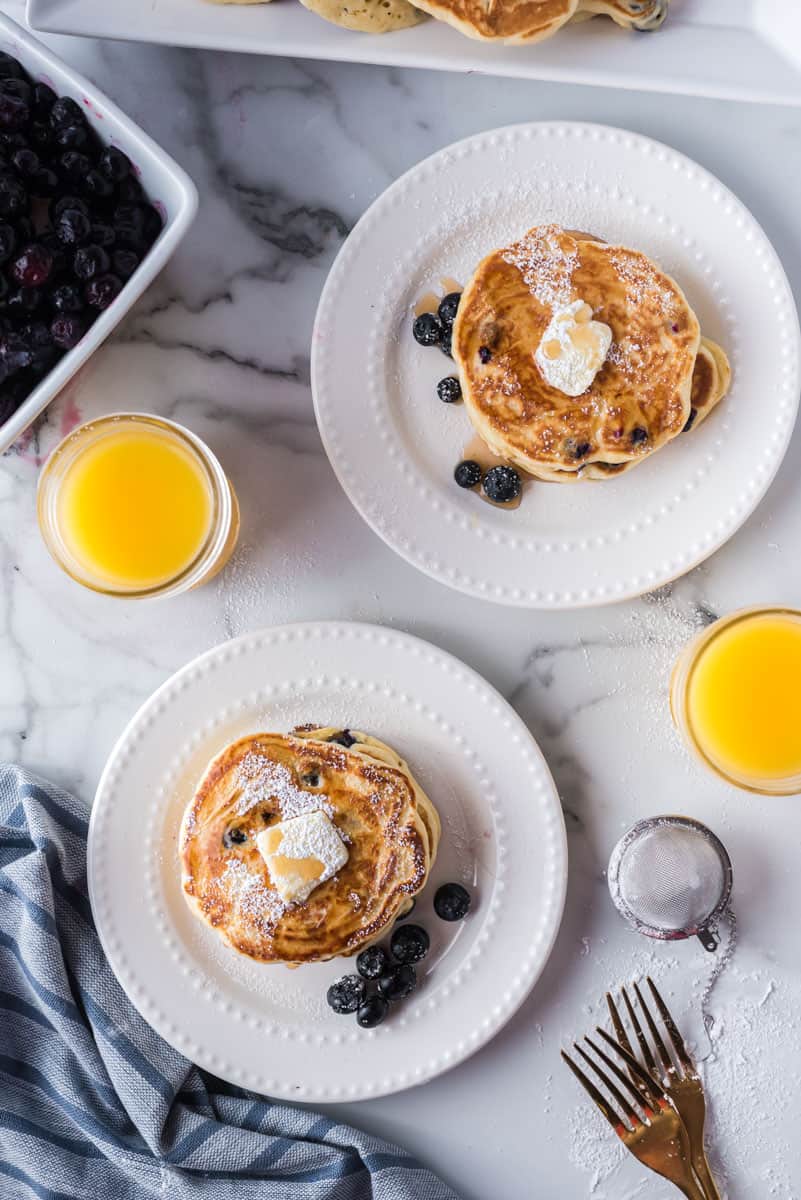 Overhead view of a breakfast for two consisting of pancakes, blueberries, and orange juice.