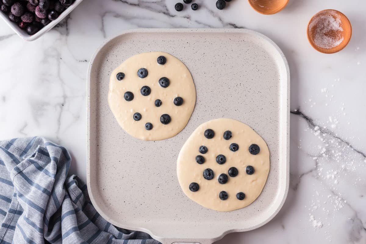 Uncooked blueberry pancakes on a griddle.