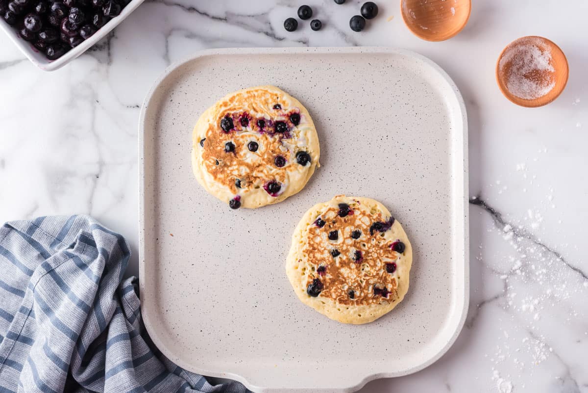 Pancakes with blueberries on a griddle.