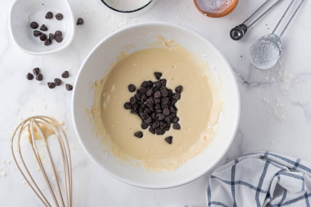 Chocolate chips added to pancake batter in a white mixing bowl.