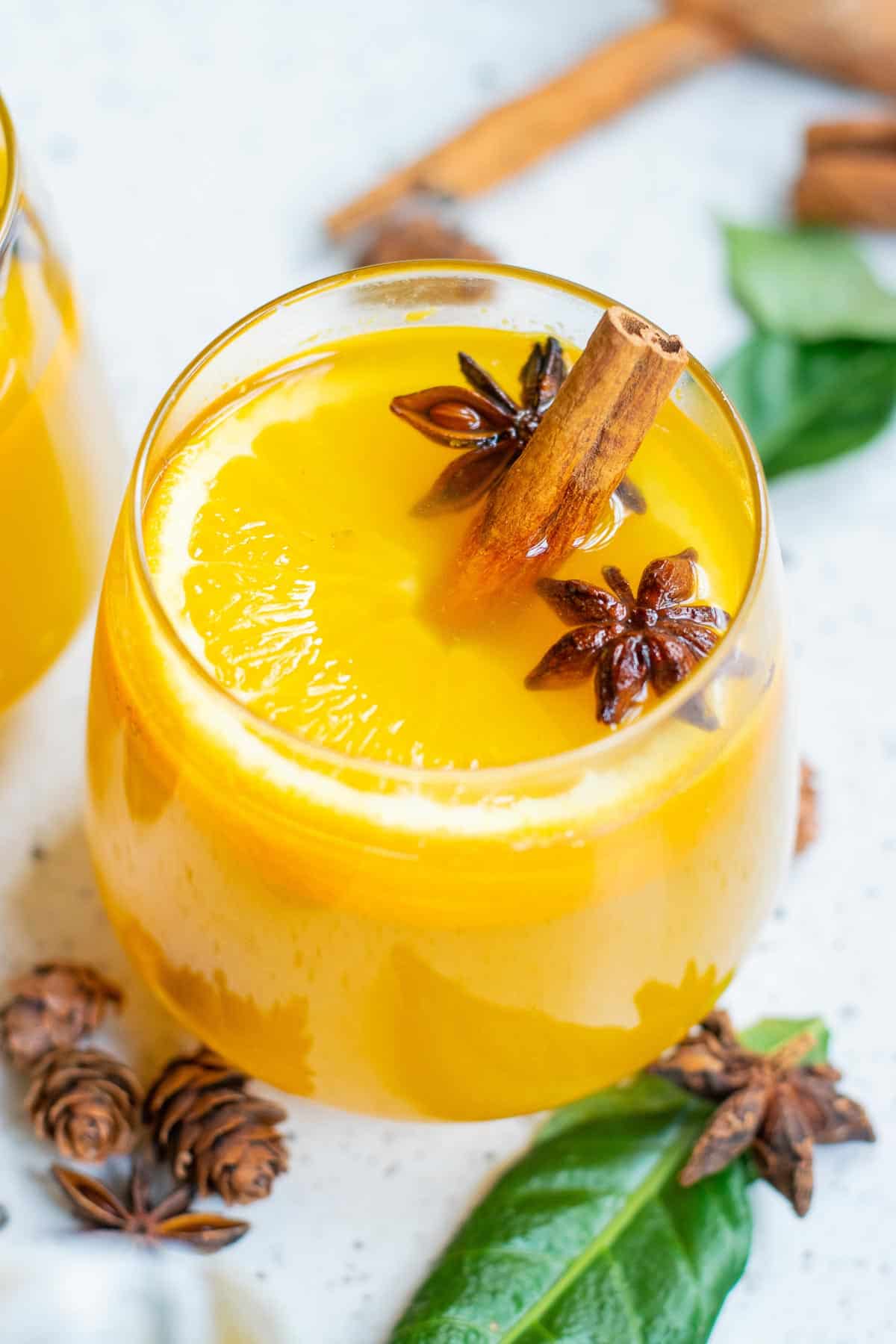 Orange punch in a wine glass with whole star anise and cinnamon sticks.