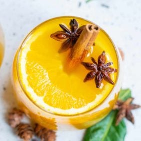 Overhead view of a bright orange warm Christmas punch garnished with star anise and cinnamon sticks.