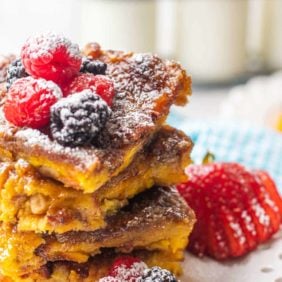 Stack of creme brulee french toast on a white plate with berries and powdered sugar.