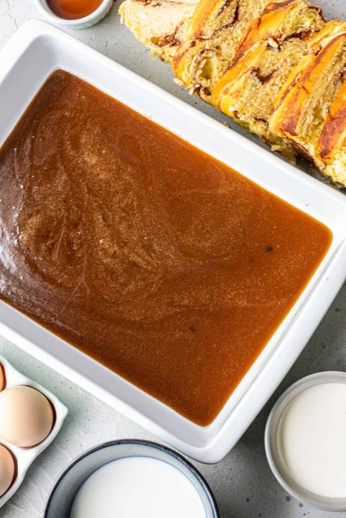 Overhead view of a white baking dish full of caramel, other french toast ingredients around the dish.
