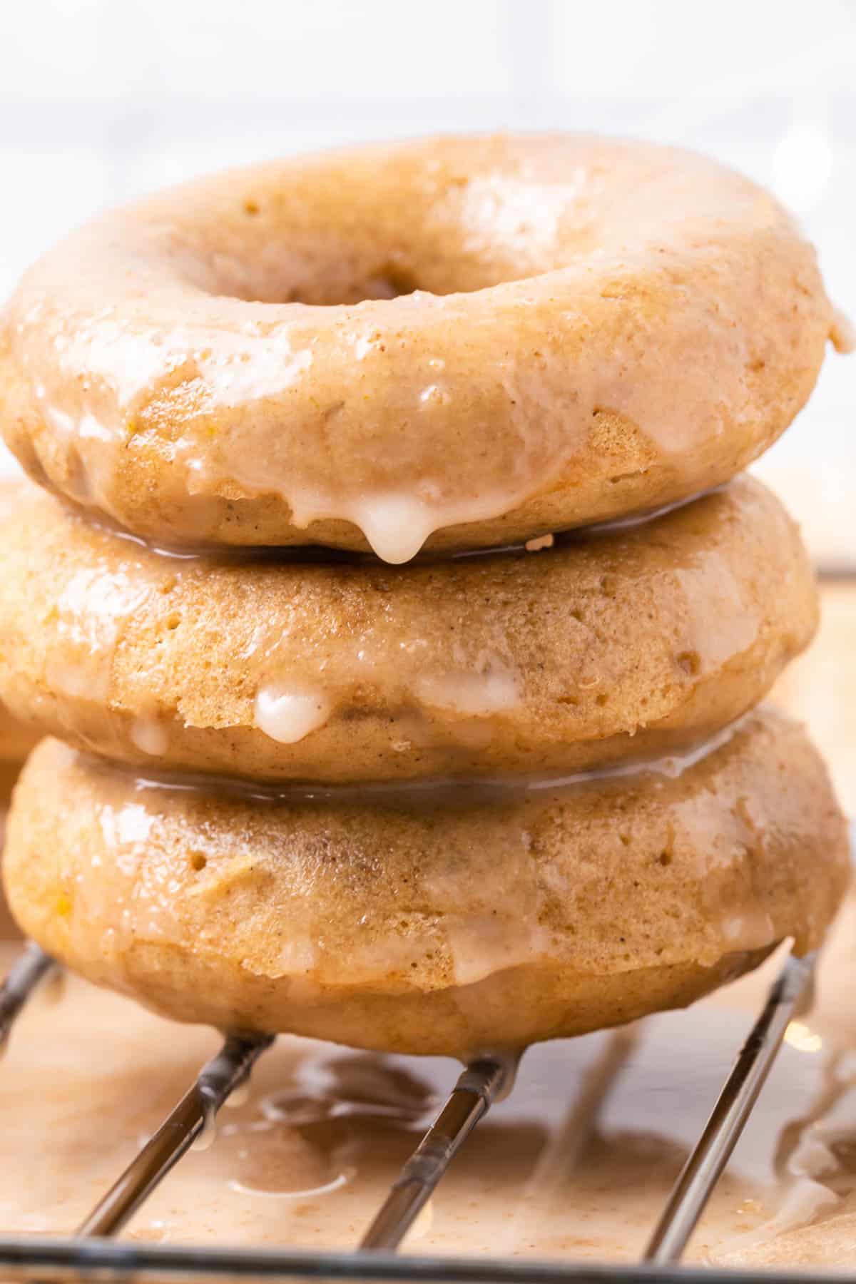 Close up of a stack of three gingerbread donuts, dripping with maple glaze.