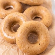 Pile of light brown donuts on a brown paper.
