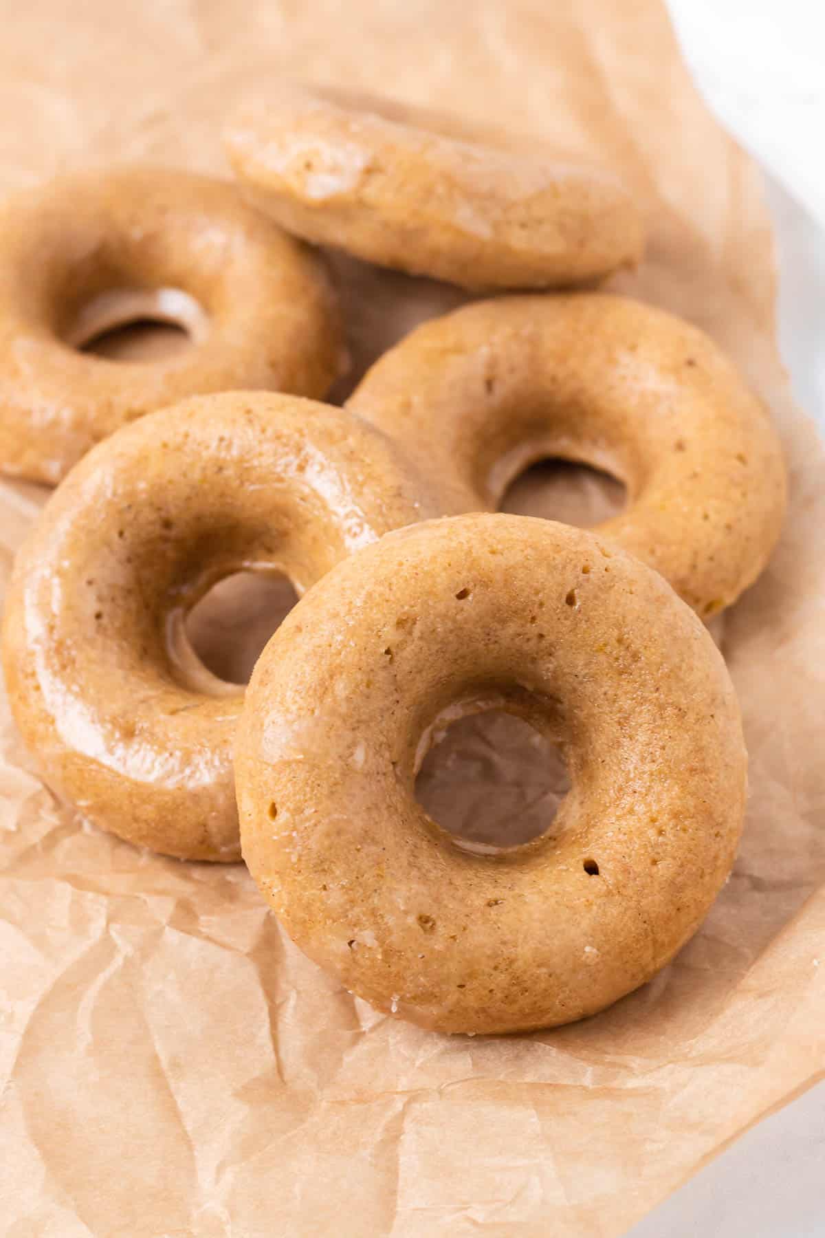 Pile of light brown donuts on a brown paper.