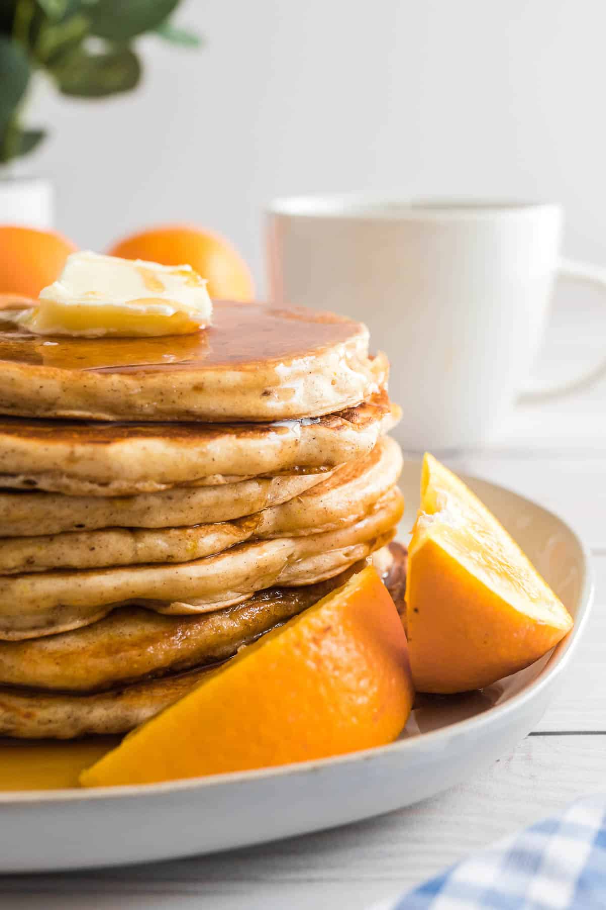 Stack of orange buttermilk pancakes on a plate with orange wedges.