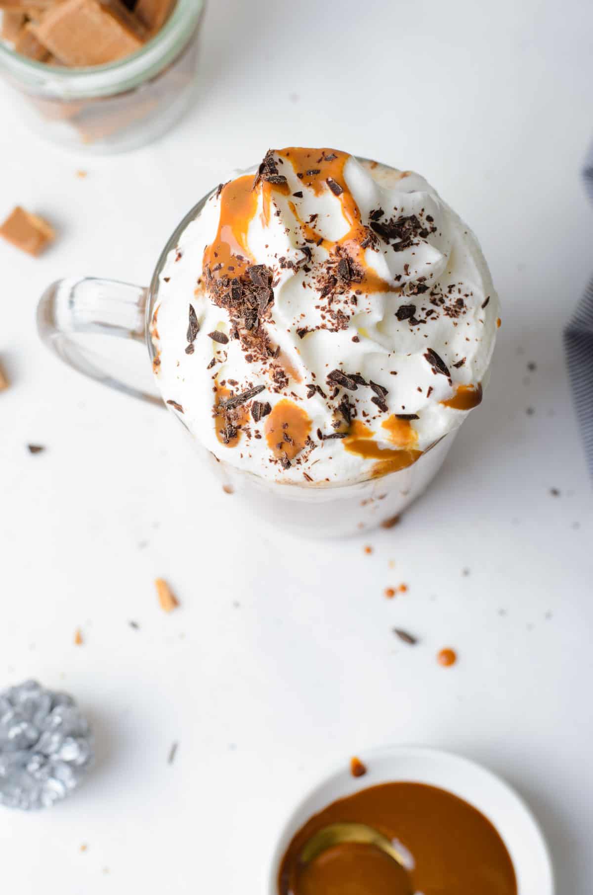 Overhead view of a mug of cocoa topped with whipped cream, caramel, and chocolate shavings.