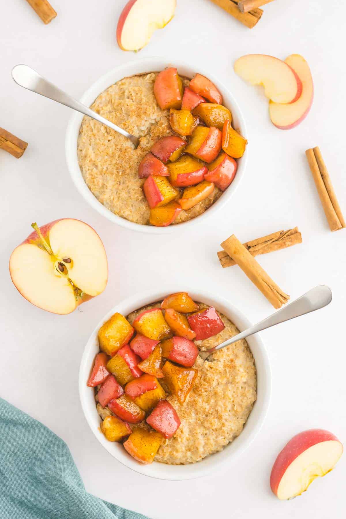 Two bowls of oatmeal topped with cooked cinnamon apples.