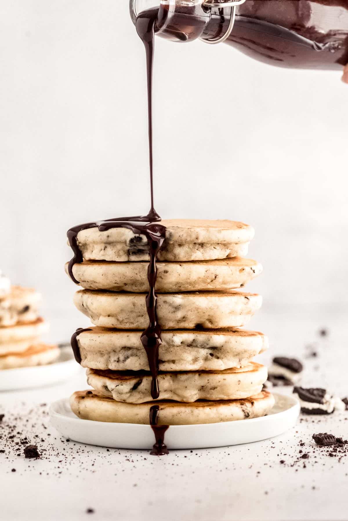Homemade chocolate syrup being poured on a tall stack of pancakes.