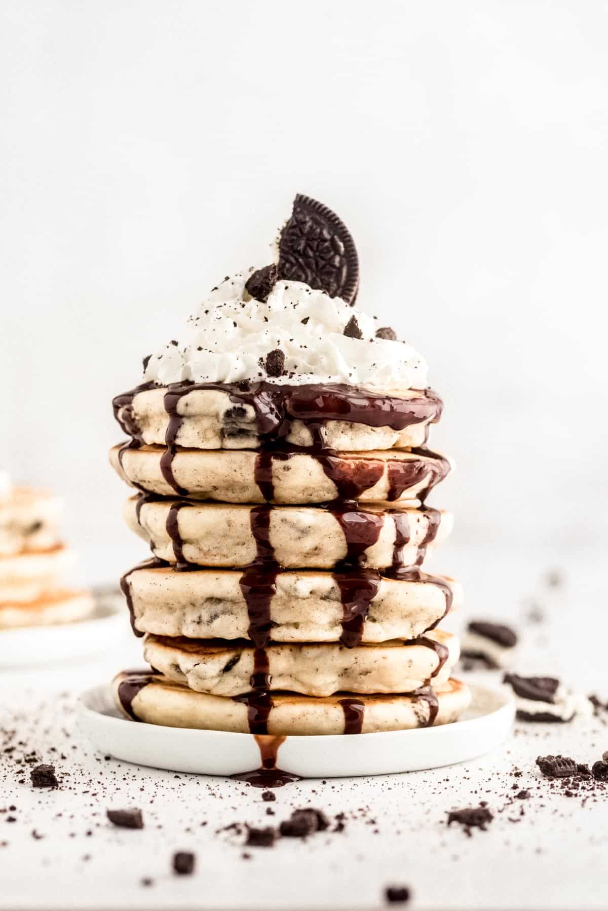 Tall stack of oreo pancakes topped with chocolate syrup, whipped cream, and crushed cookies.