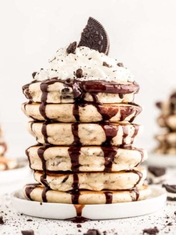Stack of oreo pancakes dripping with chocolate sauce and topped with whipped cream.