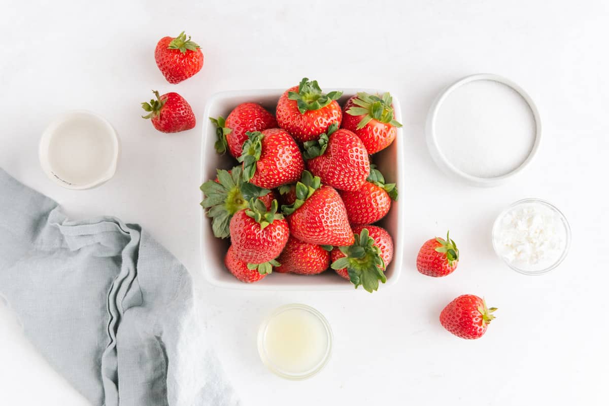 Overhead view of fresh strawberries, sugar, lemon juice, cornstarch, and water.