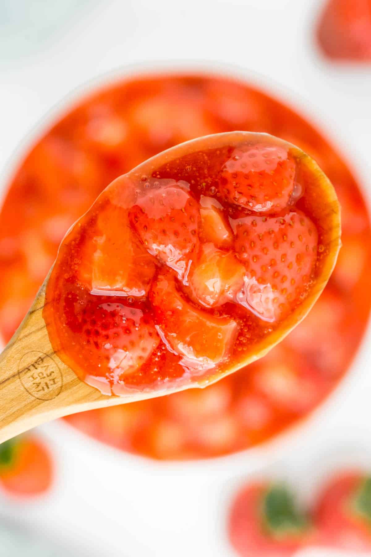 A spoon of strawberry sauce held over a bowl of more.