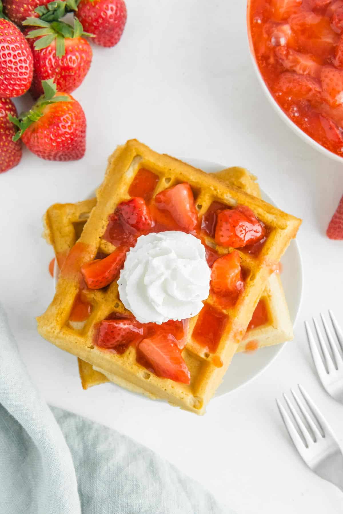 Waffles topped with strawberries and whipped cream. 