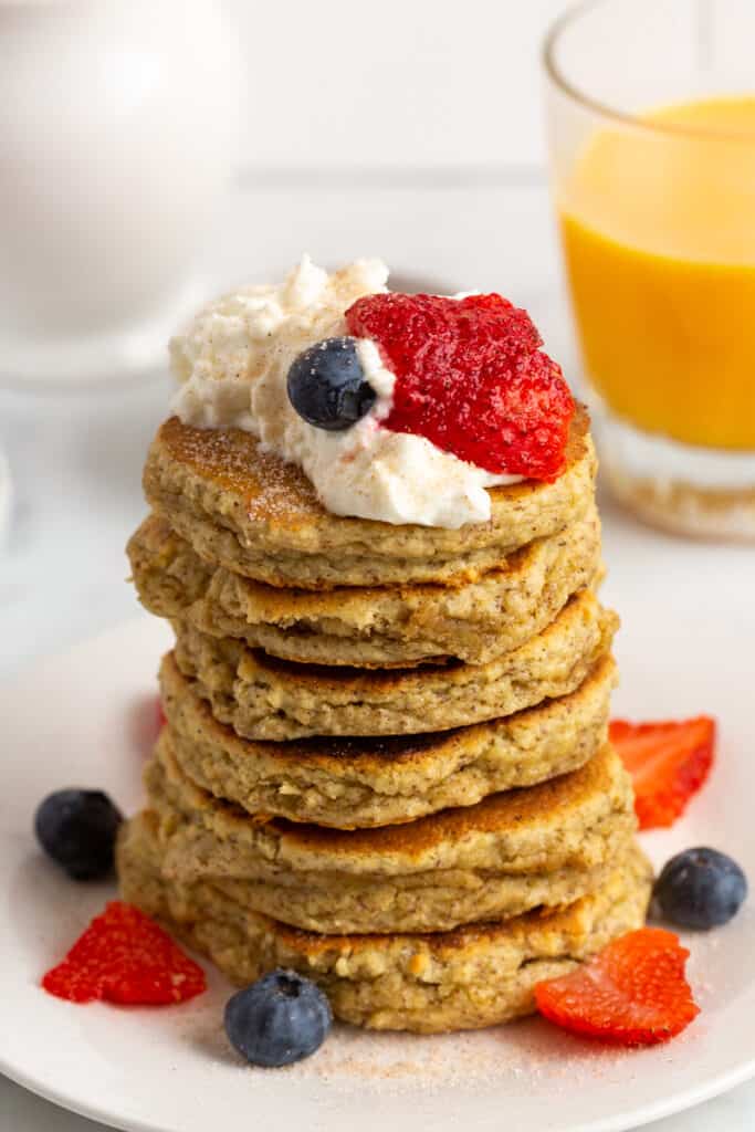 Tall stack of pancakes with berries and whipped cream.