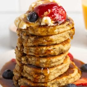 Large stack of almond flour pancakes with whipped cream and fruit and syrup.