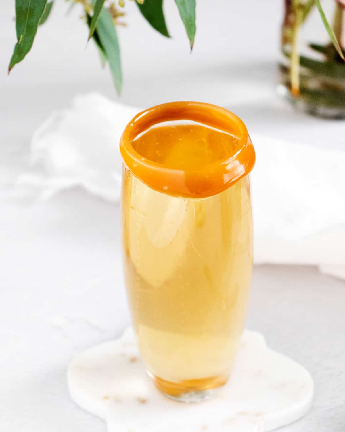 Mimosa with caramel rimmed glass on white coaster.