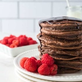 Large stack of chocolate pancakes on a plate with raspberries.