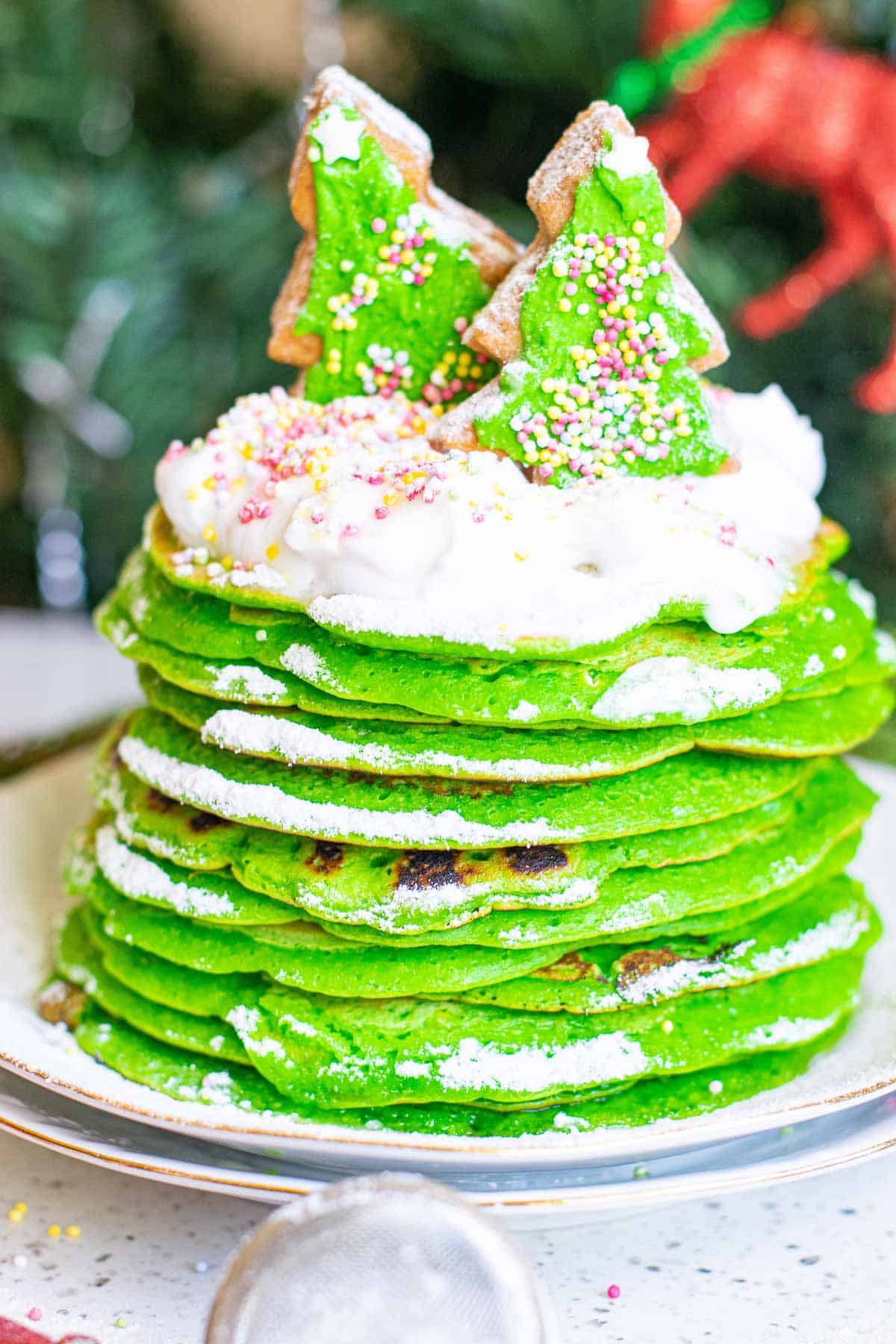 Stack of holiday pancakes with whipped cream and two sugar cookie Christmas trees on top.