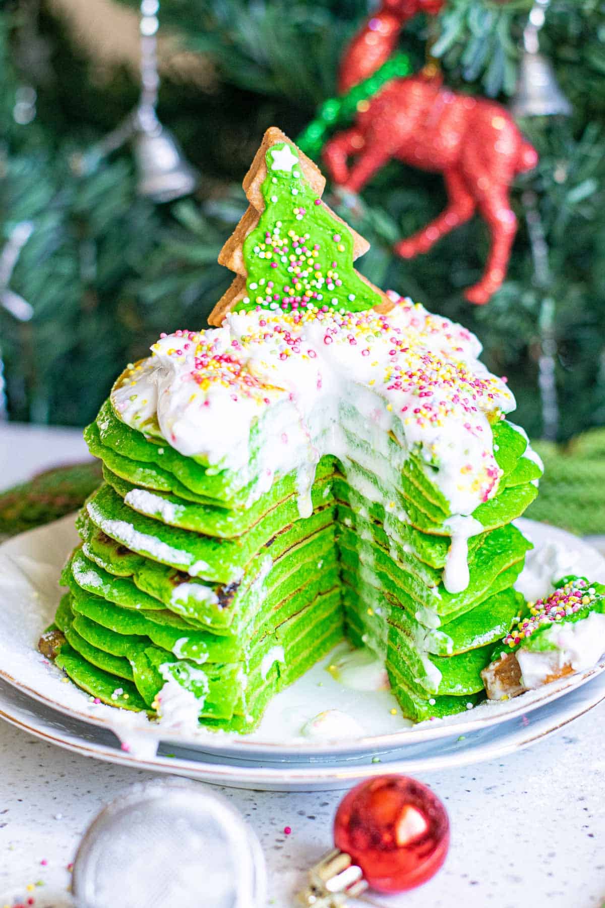 A stack of bright green pancakes with a wedge cut out to show texture. They are topped with whipped cream.