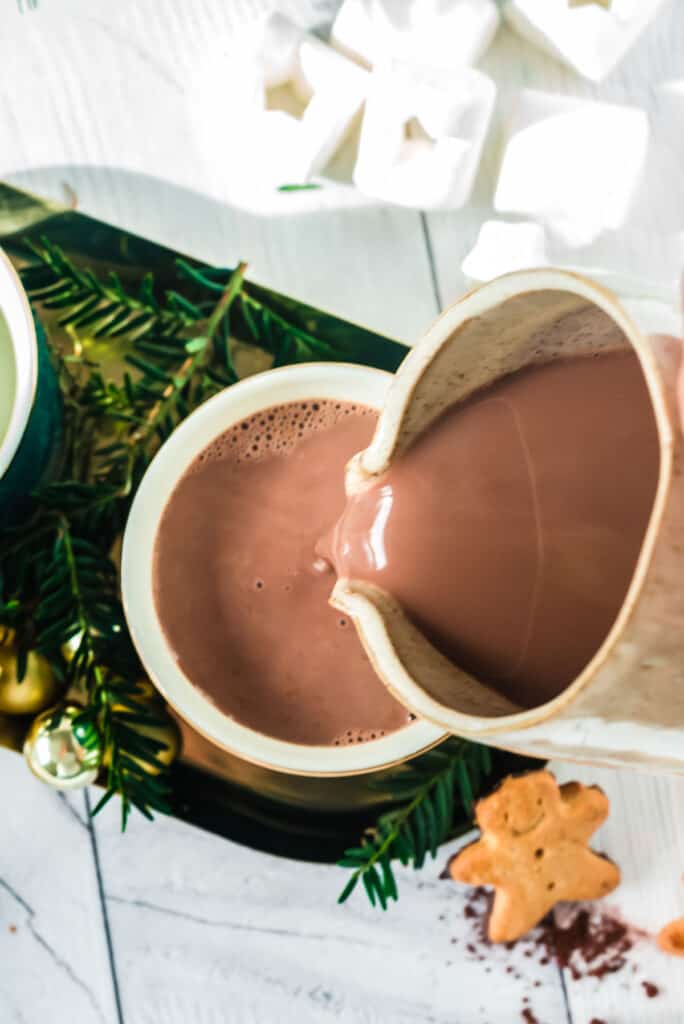 Overhead view of hot chocolate being poured into a green mug.
