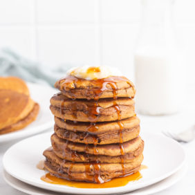 A stack of fluffy gingerbread pancakes topped with whipped cream and maple syrup.