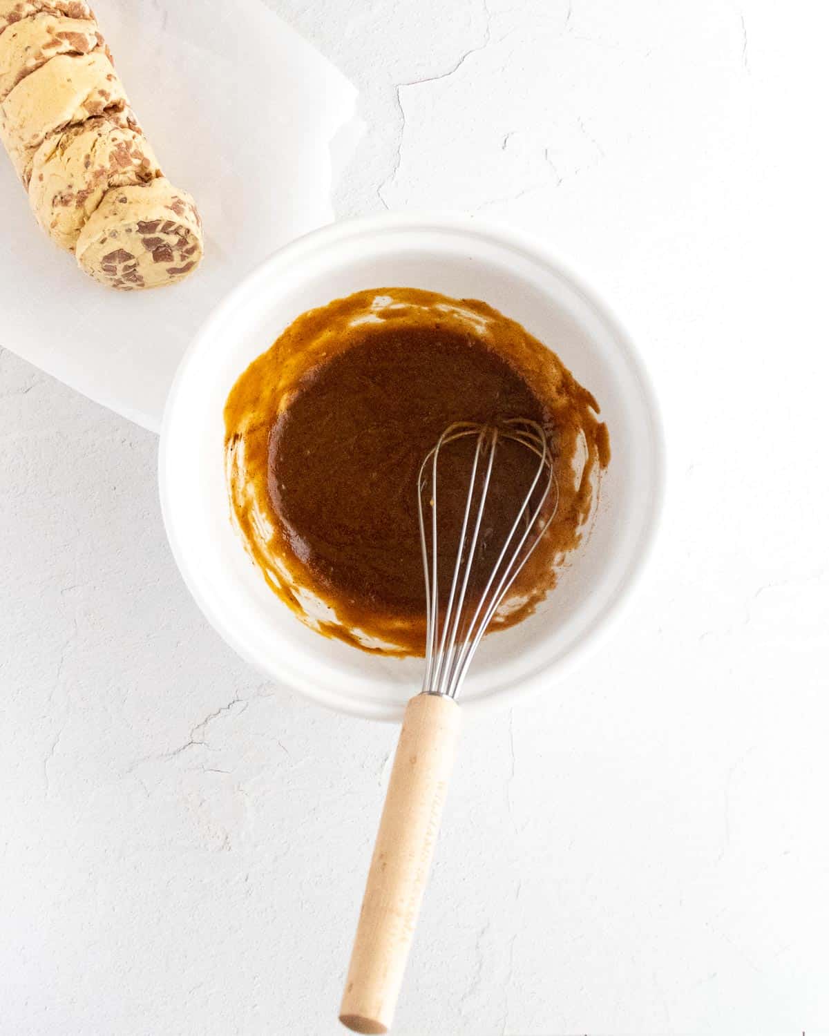 Pumpkin puree mixed with butter and brown sugar and spices in a white bowl with whisk.