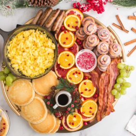 Christmas brunch board with cinnamon rolls, pancakes, scrambled eggs, meat, and fruit.