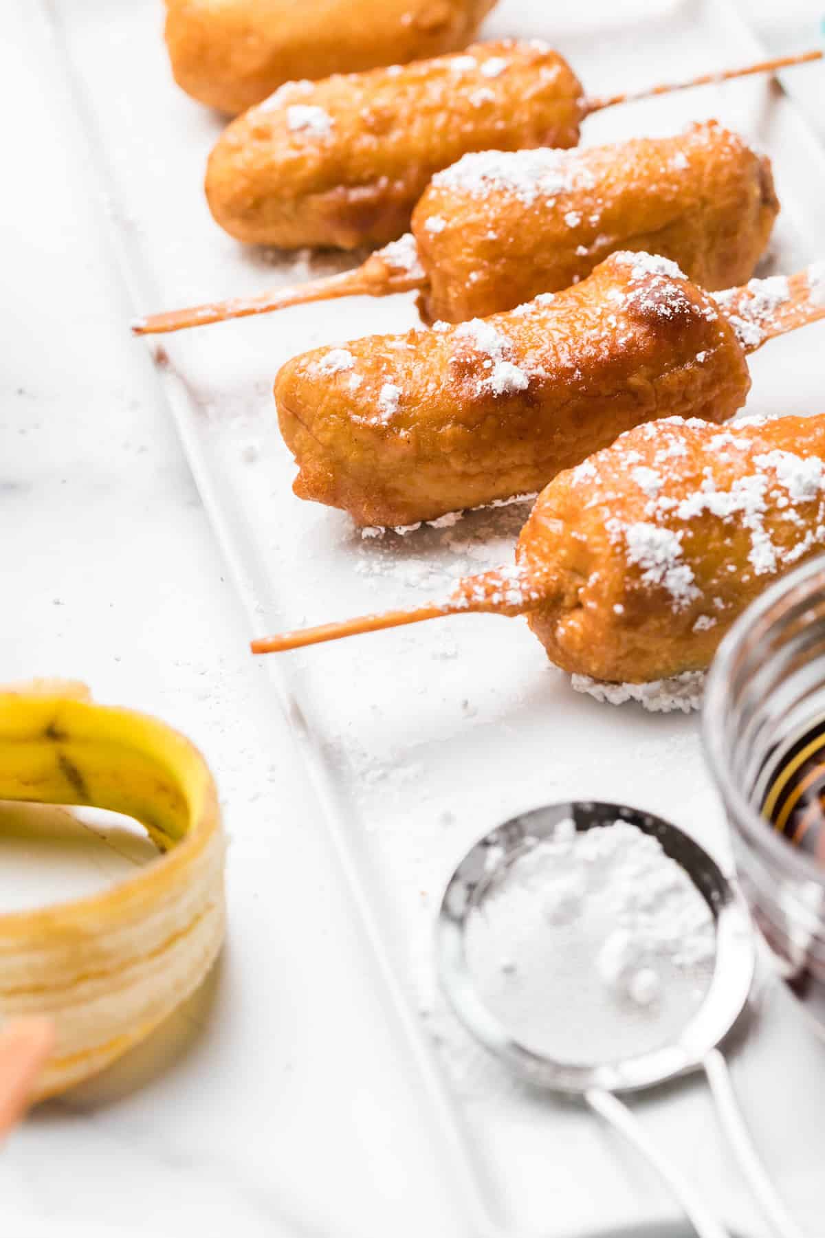 Fritters on a platter with powdered sugar and maple syrup.