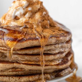 Stack of eggnog pancakes with syrup and whipped cream and cinnamon.