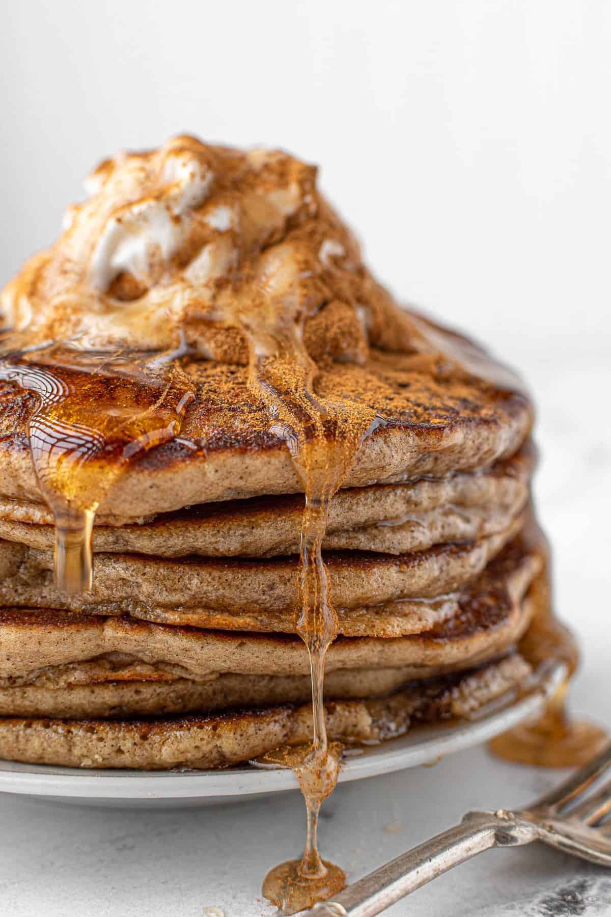 Stack of eggnog pancakes with syrup and whipped cream and cinnamon.