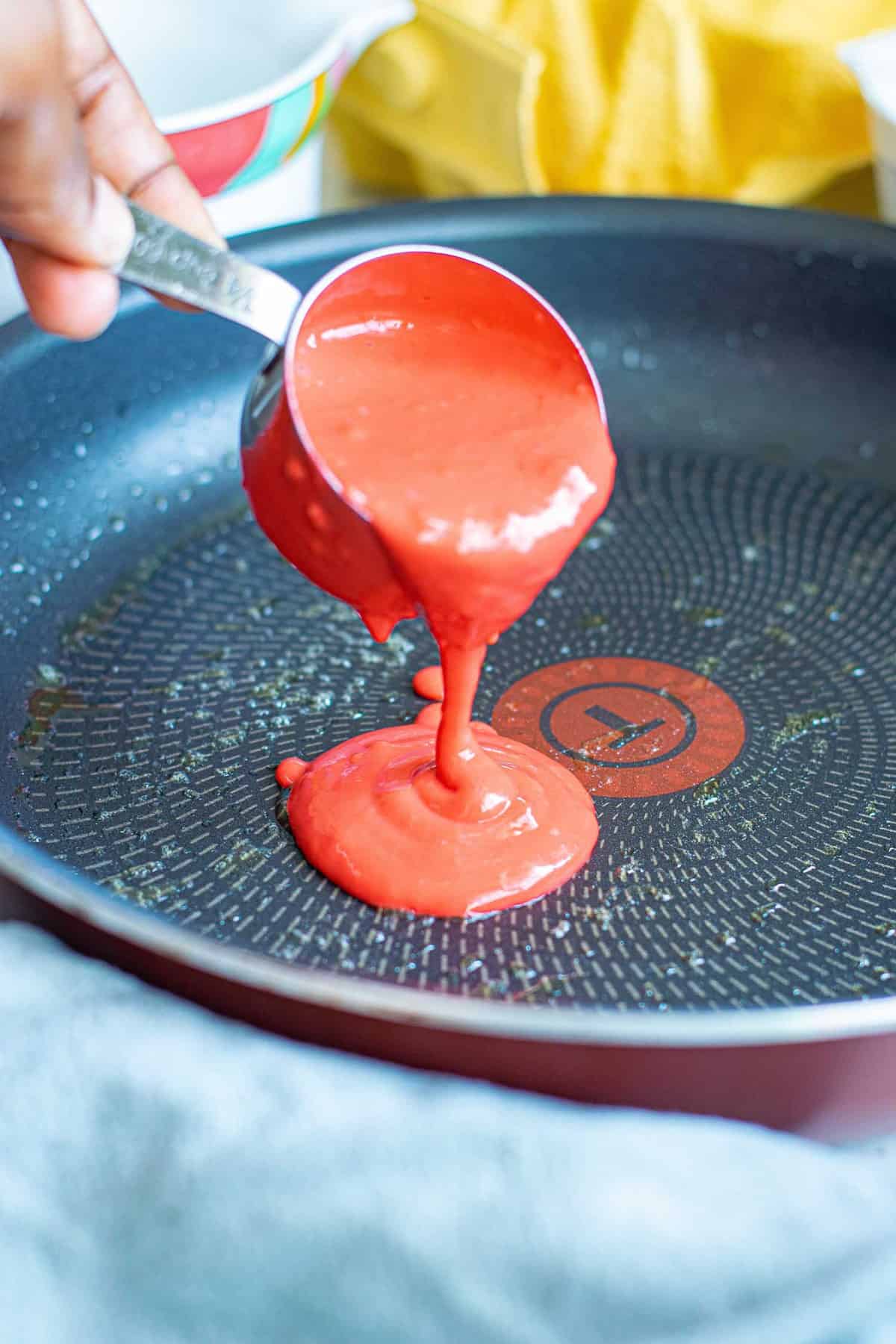 Red batter being poured onto a pan.