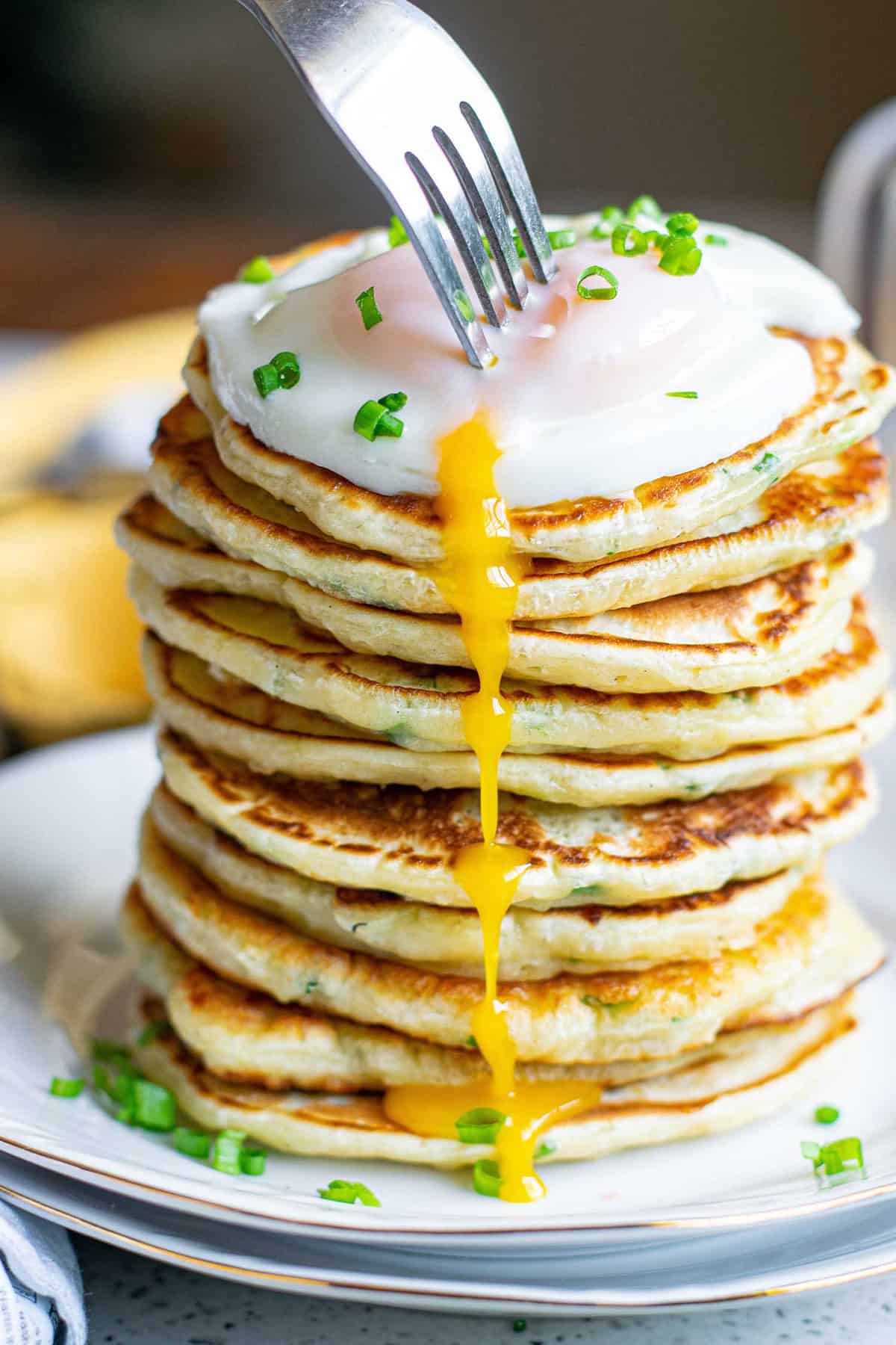A fork stabbing an egg atop a stack of pancakes, yolk running down the side.
