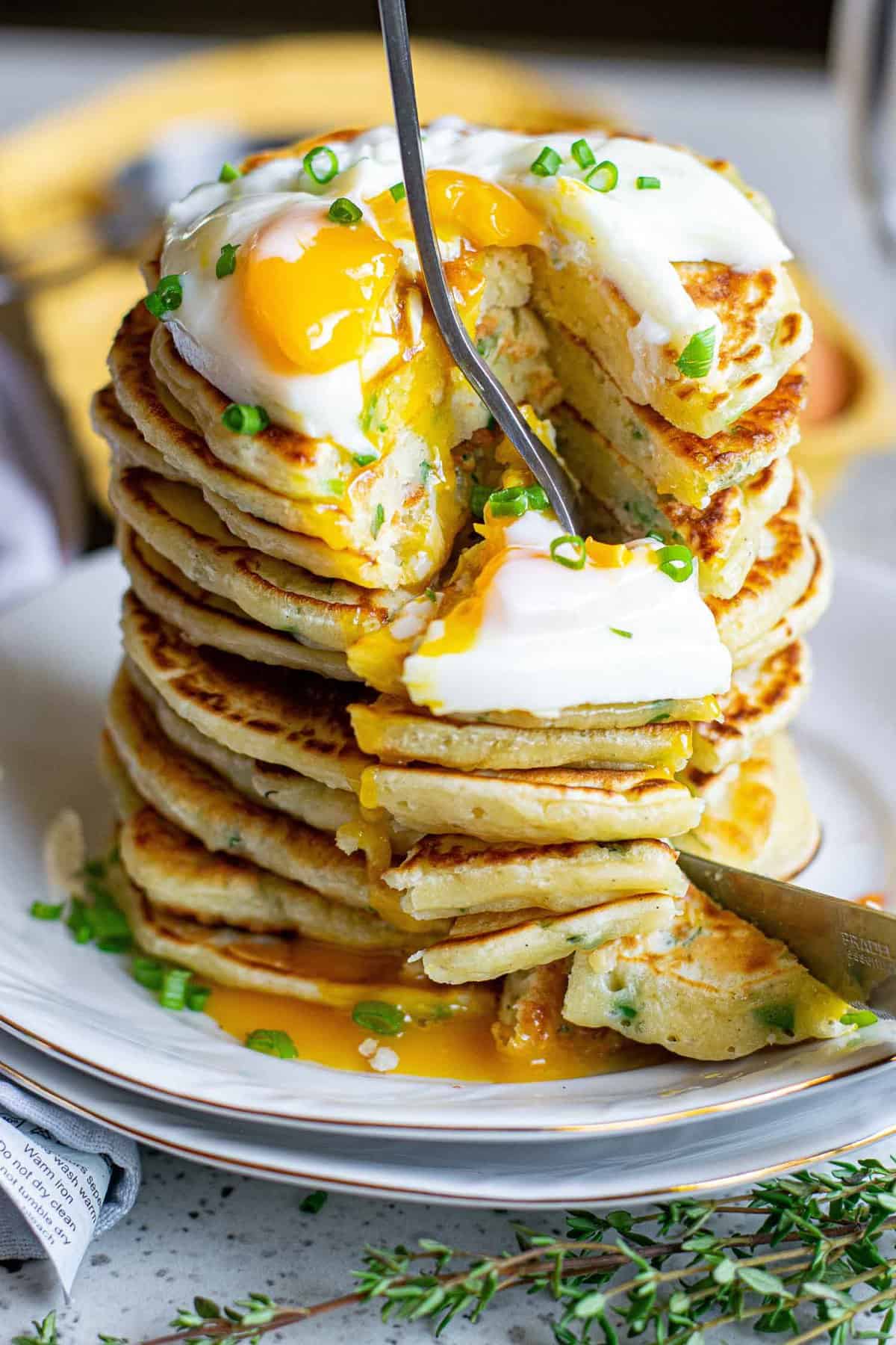 Stack of pancakes topped with an egg, being cut with a fork.