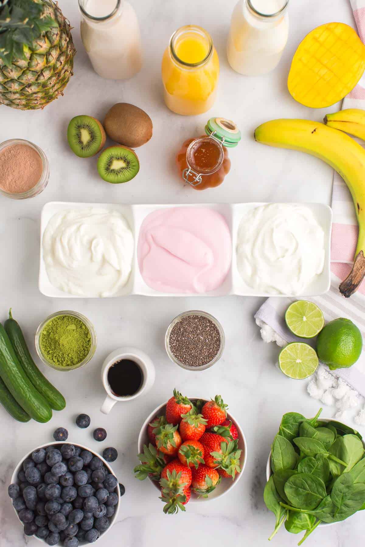 Overhead view of smoothie ingredients including yogurt, fruit, vegetables, and sweeteners.