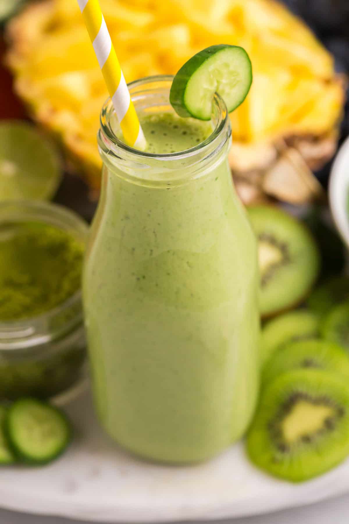 Close up of green smoothie with a yellow and white straw.